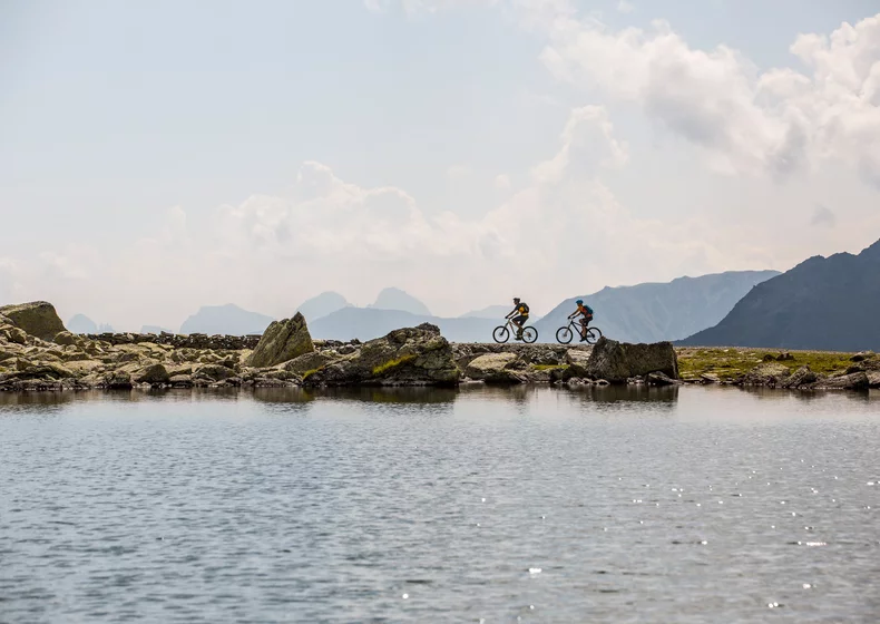 Zwei Mountainbiker fahren entlang eines Bergsees