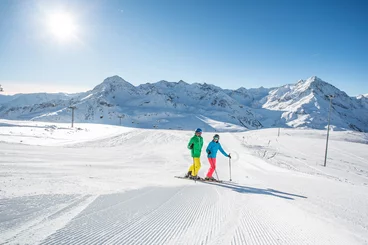 Zwei Skifahrer stehen auf einer frisch präparierten Piste bei Sonnenschein